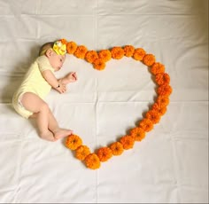 a baby laying in the shape of a heart made out of orange carnations