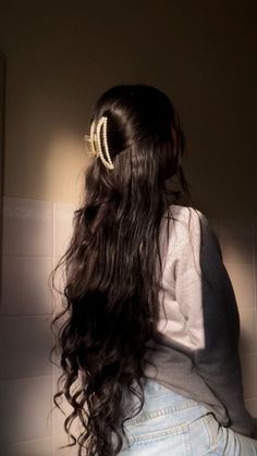 the back of a woman's head with long dark hair in a ponytail, against a white tiled wall