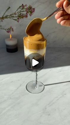 a person is spooning something into a glass with liquid in it on a marble table