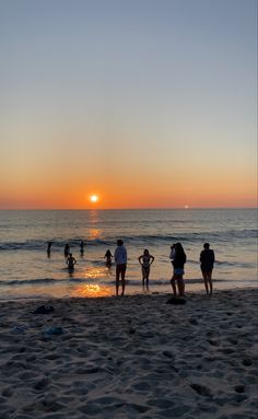 people are standing on the beach at sunset