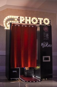 a photo booth with red curtains and lights on the wall behind it is lit up