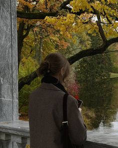 a woman is looking out at the water and trees with yellow leaves on it,