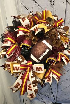 a football wreath with gold, red and white ribbons hanging on the front door or wall