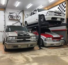 two cars are parked on top of each other in a garage with their hoods up