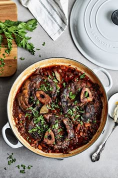 a pot filled with stew and mushrooms on top of a table next to a cutting board