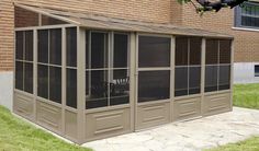 a screened in porch with chairs on the side and brick building behind it, along with green grass