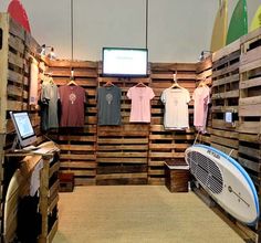 a surf shop with wooden pallets and t - shirts hanging on the wall next to it