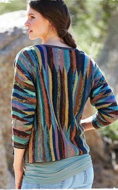 a woman wearing a multicolored knitted sweater standing in front of some rocks