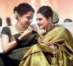 two women sitting next to each other in sari and one is holding her hand on her shoulder