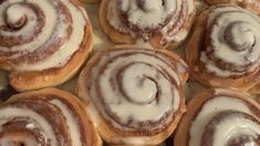 several cinnamon rolls with icing sitting on top of each other in a baking pan