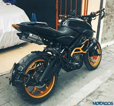 a black and orange motorcycle parked on the sidewalk next to a bed in a room