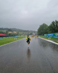 a person running in the rain with an umbrella over their head and other people walking down the road behind them