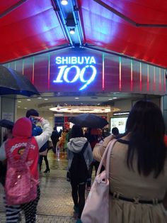 many people are walking in front of the shibuya 100 store with umbrellas over their heads