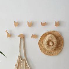 a straw hat and several wooden animals on a white wall next to a bag with a string hanging from it