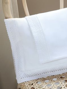 a white pillow with scalloped edges on a wicker chair next to a basket