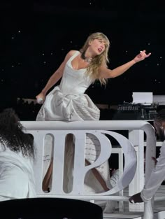 a woman in a white dress is standing on a balcony with other people around her