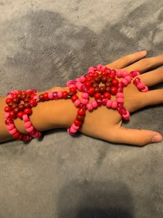 a woman's hand with pink beads and red bracelets on it sitting on a gray surface