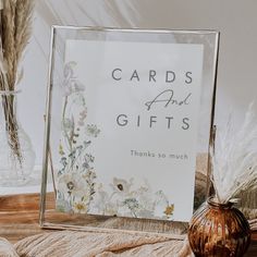 a card and gift sign sitting on top of a table next to a vase with dried flowers