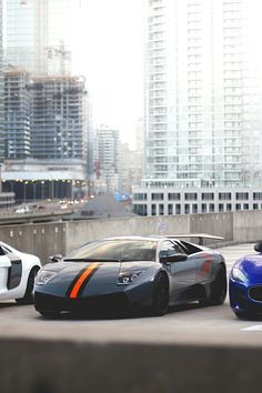 three exotic sports cars parked in front of tall buildings