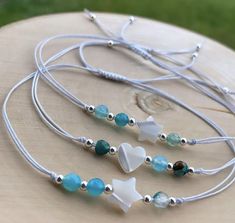 three necklaces with white, blue and green beads on a wooden table in the grass