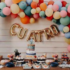 a young boy sitting in front of a cake surrounded by balloons and cupcakes