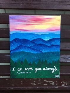 a painting on a wooden bench that says i am with you always, and mountains in the background