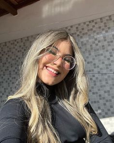 a woman with glasses and long blonde hair smiling in front of a tiled wall behind her