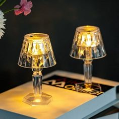 two clear glass lamps sitting on top of a table next to a vase with flowers