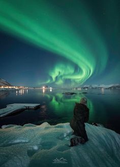 a person standing on top of snow covered ground next to an aurora bore in the sky