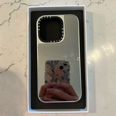 a person holding a cell phone in a box on a marble counter top with the reflection of someone's hand