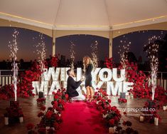 a man and woman kissing in front of a sign that says will you marry?