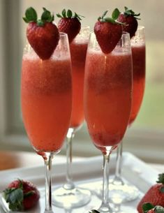 three glasses filled with liquid and strawberries on a tray