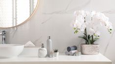 a white bathroom with marble counter tops and flowers in the vase on the sink area