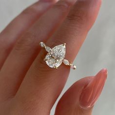 a woman's hand holding an engagement ring with a pear shaped diamond on it