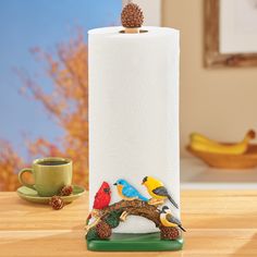 a paper towel holder with birds and pine cones on it, sitting on a table next to a coffee cup