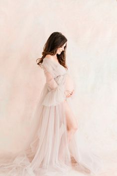 a pregnant woman in a white gown poses for the camera with her legs spread out