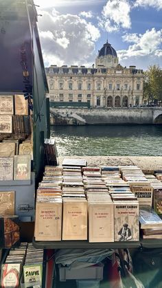 many books are stacked on top of each other near the water and a building in the background