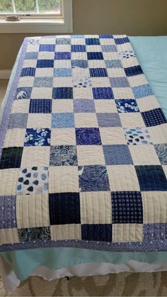 a blue and white quilt sitting on top of a bed next to a window in a bedroom