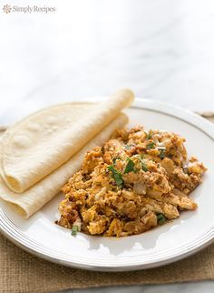 a white plate topped with food next to a tortilla on top of a table