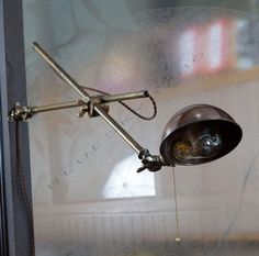 an old fashioned desk lamp is hanging on the glass wall in front of a window