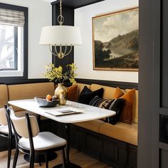 a dining room table with two chairs and a bench in front of it, next to a painting on the wall