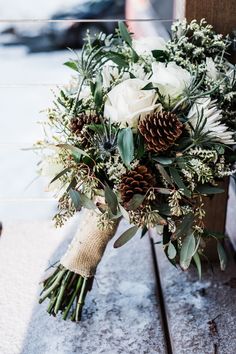 a bridal bouquet with white flowers and greenery on a wooden bench in the snow