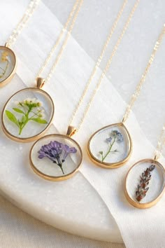 four necklaces with pressed flowers in them on a white tablecloth and gold chain