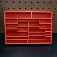 a red plastic shelf with several compartments on it and holes in the wall behind it