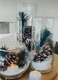 two glass vases filled with pine cones and candles on a table next to each other