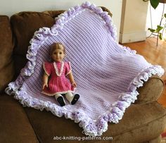 a crocheted blanket with a doll sitting on top of it in front of a couch