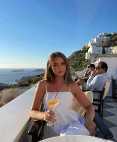 a woman holding a glass of wine sitting on top of a table next to the ocean