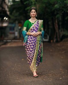 a woman in a purple and green sari is walking down the street with her hands on her hips