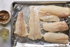 raw fish sitting on top of tin foil next to seasoning and salt in small bowls