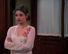 a woman with her arms crossed standing in front of a door wearing a pink dress